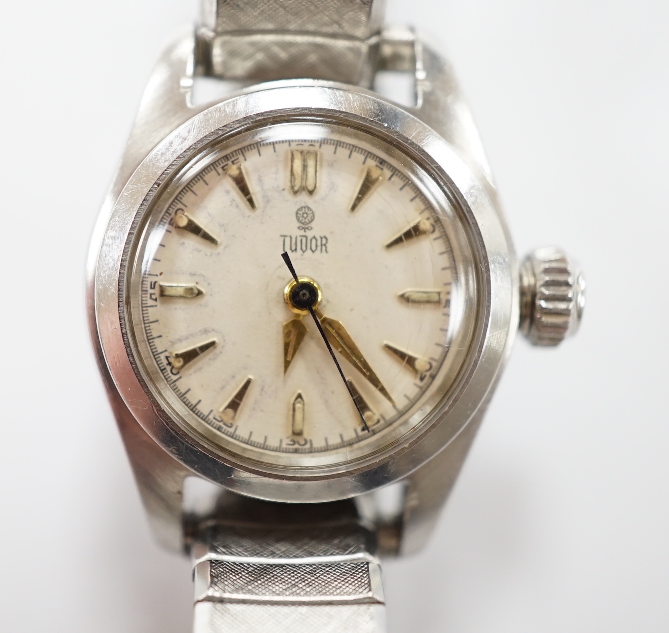 A lady's stainless steel Tudor manual wind wrist watch, with baton numerals, on an associated flexible bracelet.